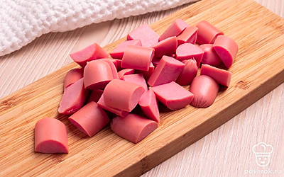 Сосиски очистите. Разрежьте сначала пополам, затем каждую половинку на произвольные кусочки. Каждую дольку чеснока очистите от кожуры и мелко порежьте. Помидоры порежьте на мелкие квадратики. Кожуру снимать не обязательно.