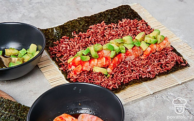 Сформируйте роллы. Циновку оберните пищевой пленкой, расстелите ее на рабочей поверхности, положите поверх лист нори. Ровным слоем выложите красный рис, немного не доходя до края. Промажьте его рисовым уксусом, свободный край нори смажьте водой. Выложите половину лангустинов, поверх них обжаренные кусочки авокадо. Сверните плотным рулетом. Аккуратно острым ножом поделите его на равные кусочки. Повторите процесс с оставшимся листом нори и начинкой.