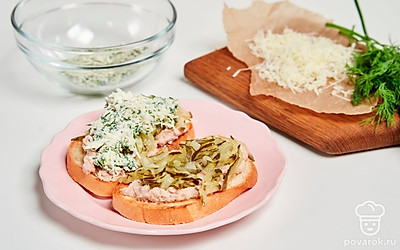 Подготовьте начинку. Натрите крупно соленый огурец и выложите поверх трески. Затем смешайте тертый сыр с нарезанным укропом и майонезом. Выложите смесь из сыра и укропа поверх соленых огурцов. Подавайте тосты холодными.