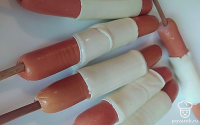 Сосиски наколите на деревянные шпажки и оберните пластинами плавленого сыра. Кляр перелейте в высокий стакан и опустите в него сосиску, чтобы кляр покрыл ее полностью.