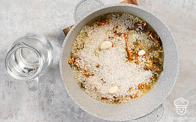 Всыпьте в казан рис. Влейте воду, чтобы она покрыла крупу, и посолите, не перемешивая. Зубчики чеснока надрежьте крест-накрест и положите поверх риса. Варите под крышкой, пока рис не впитает всю жидкость. Перед подачей дайте настояться 20 минут.