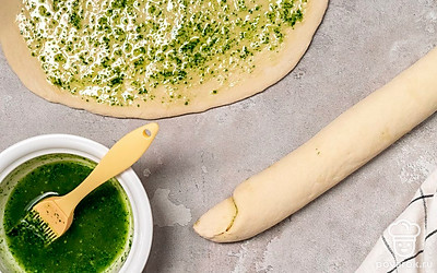 Скрутите багет. Тесто разделите на две части. Каждую часть раскатайте в тонкий пласт, смажьте половиной зеленой прослойки. Скрутите плотные рулеты, защипните края.