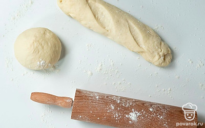 Сформируйте багет. Готовое тесто снова разомните руками, после чего разделите его на две равные части. Каждый кусок теста раскатайте в пласт толщиной не более 1 см. Затем сверните его в трубочку и положите швом вниз на противень, застеленный пергаментной бумагой. Сделайте небольшие надрезы по поверхности теста и оставьте его на 30 минут в теплом месте.