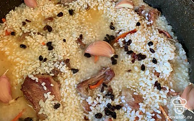 Когда мясо почти готово, выложить заранее замоченный рис. Засыпать специи, добавить зубчики чеснока, и самое главное — выложить барбарис. Залить водой на 1-2 сантиметров выше риса. Поставить на минимальный огонь и закрыть крышкой. 