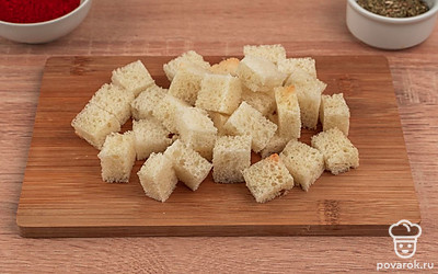 Возьмите пшеничный хлеб и выложите его на разделочную доску. Срежьте хлебную корочку и нарежьте мякиш на квадратики среднего размера.