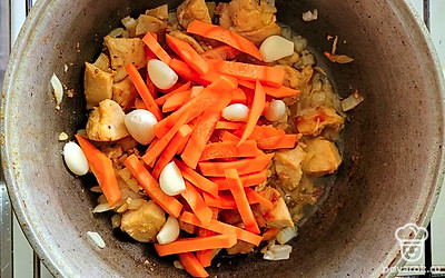 Добавьте лук, морковь и зубчики чеснока в казан к курице. Жарьте все вместе 5-7 минут.