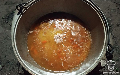 В казан засыпьте рис, но не перемешивайте. В середину пристройте головку чеснока. Тушите опять под крышкой, до готовности риса. Томите ориентировочно еще минут 10-15.