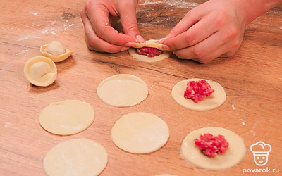 Слепите пельмени. Достаньте тесто из холодильника, разрежьте на 2 части и раскатайте каждую толщиной 2-3 мм. Вырежьте рюмкой кружочки, положите на них фарш и слепите тесто по краям.