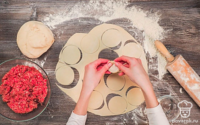 Начните готовить первую порцию пельменей. Отщипните от общего куска тесто размером примерно с кулак. Добавьте немного муки и разомните 1-3 минуты. Засыпьте рабочую поверхность мукой. Раскатайте тесто толщиной около 2-3 мм. Возьмите рюмочку и вырежьте кружки диаметром 4-6 см. Выложите на кружочек готовый мясной фарш и плотно слепите тесто по краям. Проделайте то же самое с остальными частями теста и фарша.