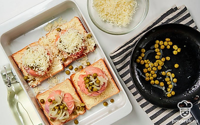 Запеките тосты. На ломтики хлеба уложите кольца сосисок, в них выложите лук с горошком. Посыпьте сыром, запеките в течение 7-10 минут в духовке.