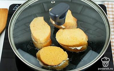 Раскалите сковороду с небольшим количеством растительного и сливочного масла, выложите гренки с творожной начинкой. Накройте крышкой и оставьте жариться в течение 4 минут.