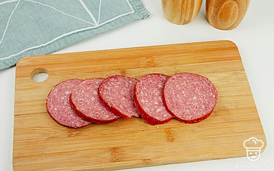 Нарежьте тонкими кусочками колбасу и батон.