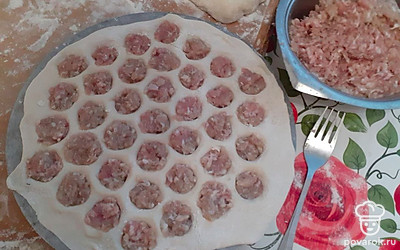 Выложите тесто на пельменницу, в каждую ячейку положите немного мясного фарша.