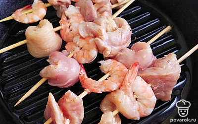 На половину шпажек наденьте куски курицы и креветки, чередуя все между собой. На другие шпажки наденьте куски свинины и курагу. Обжарьте шпажки на сковороде гриль 7-10 минут.