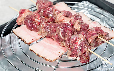 Пожарьте шашлык. Проложите противень фольгой. Сверху на противень поместите решетку духовки, выложите на неё кусочки сала. Нанизывайте говядину на шпажки, помещая куски не слишком плотно. Положите шпажки с мясом на кусочки сала и поставьте в духовку на 15-25 минут. Переворачивайте шпажки и следите, чтобы мясо не горело и не зарумянилось в первые минуты готовки.