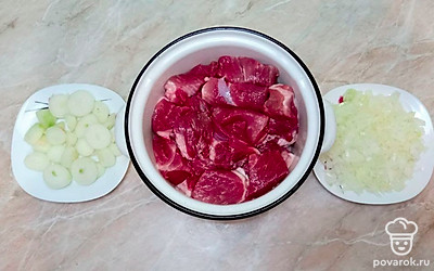 Лук очистите. Две луковицы нарежьте мелко ножом или измельчите при помощи блендера, а остальной лук нарежьте кольцами. Нарежьте мясо кусками среднего размера и сложите в емкость.