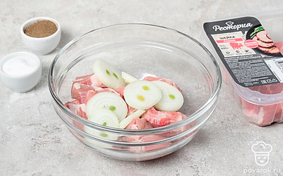 Нарежьте свинину на небольшие кусочки и выложите в миску. Измельчите лук кольцами и добавьте к мясу. 