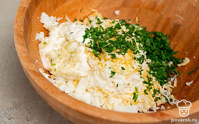 Приготовьте начинку. В миску выложите измельченный чеснок и ложку майонеза. Затем добавьте натертые яйца и тщательно размешайте начинку.