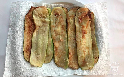 Нарежьте кабачок тонкими пластинками. Каждую пластину обмакните в муке и обжарьте на заранее разогретой сковороде до золотистой корочки. Разложите пожаренные кабачки на салфетку и оставьте их остужаться.