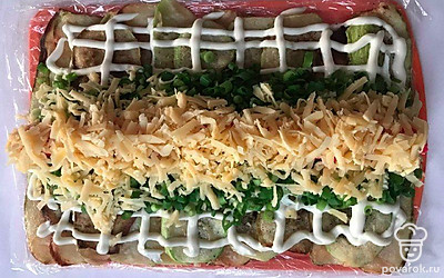 Крабовые палочки в целом состоянии выложите сверху зеленого лука - в ряд. Твердый сыр натрите на терке и выложите на крабовые палочки.