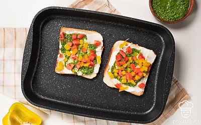 Подготовьте бутерброды к запеканию. На ломтики хлеба намажьте слой творожного сыра. Затем выложите и распределите по поверхности тоста соус песто. Добавьте нарезанный перец, помидоры. Выложите тосты на противень или на решетку на расстоянии друг от друга.