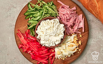 Подготовьте продукты для сэндвича. Яйца, колбасу, огурец, помидоры нарежьте соломкой. Переложите готовые ингредиенты в миску, добавьте размятую «Фетаксу» и тщательно перемешайте.