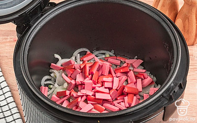 Добавьте в чашу мультиварки сосиски. Жарьте их вместе с луком до румяного оттенка.