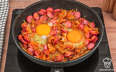 К сосискам и овощам добавьте два куриных яйца. Всё перемешайте и жарьте еще несколько минут до готовности яиц.
