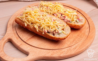 Выложите ингредиенты из тарелки в получившиеся лодочки из багета. Посыпьте тертым сыром.