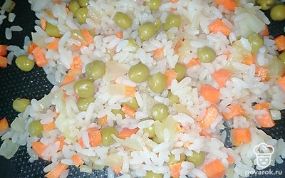 Когда подрумянятся, добавляем отваренный рис и консервированный зеленый горошек. Все перемешиваем и еще слегка обжариваем.