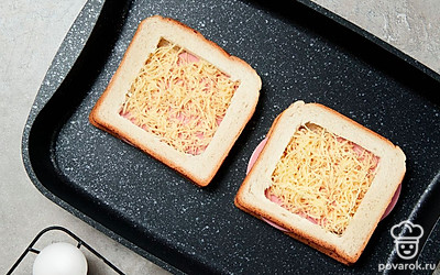 Сделайте заготовку. На противень выложите два целых ломтика хлеба. Поверх уложите ломтики колбасы, посыпьте сыром, сверху накройте кусочками с вырезанной серединой.
