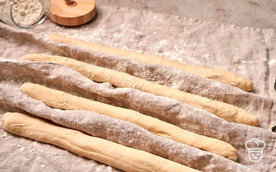 Разогрейте духовку до 250 градусов. В это время сформируйте багеты: каждую часть теста аккуратно руками растяните в жгут нужной длины. Выложите на присыпанное мукой полотенце, приподнимите полотенце между багетами, создав перегородки. По краям подложите опору. Оставьте на 30 минут.