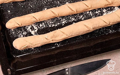 Испеките багеты. Противень присыпьте мукой, выложите на него багеты, сделайте наискосок несколько надрезов острым ножом. В небольшой противень налейте кипяток и поставьте его на дно духовки. Первые 10 минут выпекайте багеты с паром. Затем уберите противень с водой и выпекайте еще 10 минут.