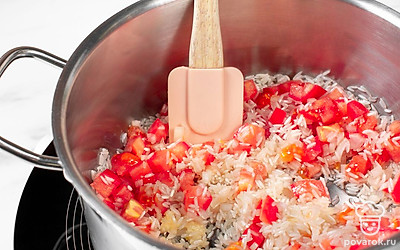 Добавьте к рису чеснок, лук и помидор. Перемешайте, а затем тушите блюдо еще 3 минуты.