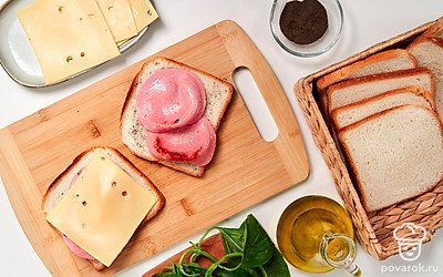 Оформите тосты. Докторскую колбасу обжарьте на сухой сковороде до золотистого цвета с двух сторон по 2 минуты. Выложите ломтики хлеба на доску, присыпьте перцем, положите колбасу и сыр.