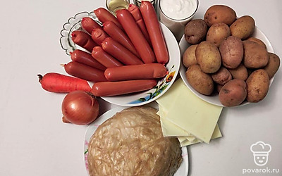 Промойте, почистите картофель, а затем натрите на терке. Снимите с сосисок оболочку. Мелко нарежьте лук и морковь. Духовку разогрейте до 180 ℃.