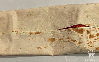 Посыпьте корейской морковью. Скрутите лаваш и выложите на противень с пергаментом. Поставьте противень в разогретую духовку на 200 °C на 10минут, переверните и поставьте еще на 7 минут.