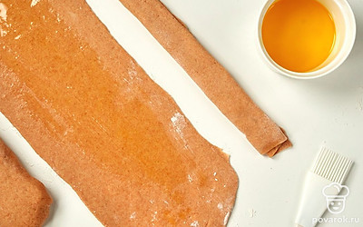 Сделайте из теста багеты с топленым маслом. Разделите тесто вручную на три части. Каждую порцию посыпьте мукой, раскатайте в прямоугольный тонкий пласт. Смажьте расплавленным топленым маслом. Сложите края к центру, затем снова к центру. Уберите три заготовки в холод на 25 минут.