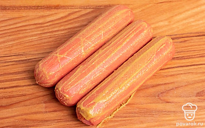 Сделайте на сосисках неглубокие крестовые надрезы по всей длине. Благодаря этому блюдо получится красивым. Смажьте сосиски горчицей по вкусу. Также промажьте горчицей и надрезы внутри.