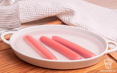 Выложите сосиски в глубокую тарелку или емкость с бортиками. Посуда обязательно должна быть подходящей для приготовления в микроволновке, например, стеклянной, керамической или из устойчивого к нагреванию пластика. Залейте сосиски стаканом горячей воды.