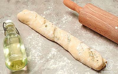 Подготовьте багеты к выпеканию. После того, как тесто подойдет, выложите его на рабочую поверхность с мукой. Раскатайте тесто в прямоугольный пласт и распределите по нему смесь из сушеного орегано и оливкового масла. Сверните пласт в рулет и закрепите тесто по краям. Сделайте сверху косые надрезы вдоль всего багета. Поставьте тесто в теплое место на 30 минут, не забыв накрыть влажным полотенцем.