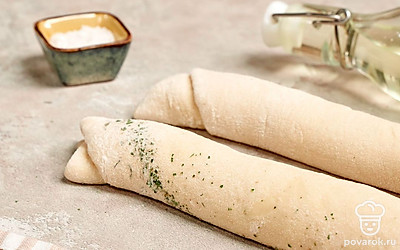 Сформируйте багеты. Достаньте тесто и разложите на рабочей поверхности, слегка присыпанной мукой. Разделите на две равные части. Из каждого кусочка сформируйте овальные лепешки. Накройте тесто пищевой пленкой на 10 минут, а затем смажьте смесью из сухой петрушки и оливкового масла. Скатайте тесто в рулеты. Уложите будущие багеты на противень на расстоянии 3 см друг от друга. Накройте полотенцем на 10 минут.