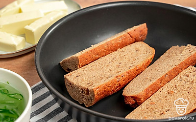 Подготовьте багет. Багет разрежьте поперек. Каждую половину разделите на две продольные части. Обжарьте на сковороде с маслом около 2-3 минут, дайте остыть.