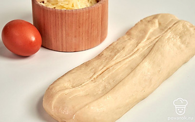 Сформируйте багеты. Подошедшее тесто слегка промните руками. Затем разделите на равные кусочки весом примерно по 80 г. Из готовых кусочков сделайте "колобки". Каждую порцию теста раскатайте в плоский прямоугольник. Скрутите в плотную трубочку, края защипните. Все заготовки выложите на противень, застеленный бумагой для выпечки. Накройте полотенцем и оставьте на 20 минут.