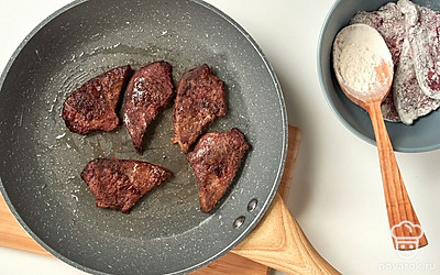 Приступите к приготовлению печени. В тарелку насыпьте муку для обвалки. Кусочки печени запанируйте в муке. Разогрейте сковороду с 2 ст. л. масла. Выложите в масло печень, посолите и обжарьте по 1 минуте с каждой стороны. Чтобы проверить готовность, проткните печень с помощью деревянной шпажки. Если выделится прозрачный сок, печень готова. Нарежьте печень ломтиками.