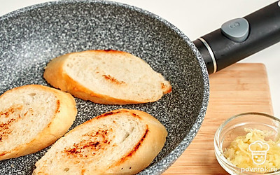 Сделайте основу для бутербродов. Багет порежьте на ломтики 2 см толщиной. Смажьте каждый кусочек тонким слоем сливочного масла с двух сторон. Разогрейте сухую сковороду и обжарьте кусочки хлеба. Выкладывайте их на тарелку, дайте слегка остыть и после этого натрите багет чесноком.