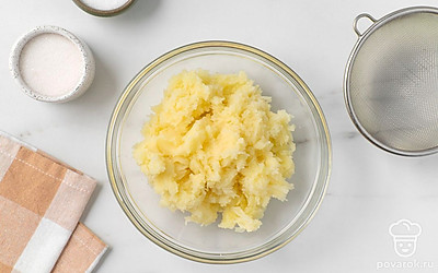 Уменьшите огонь до среднего и варите картофель в течение 15-20 минут до готовности. Слейте из кастрюли воду и дайте картофелю немного остыть. Небольшими порциями выложите картофель в сито и протрите его лопаткой в миску.