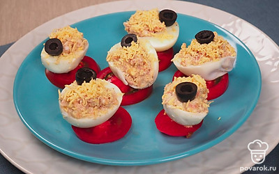 Фаршированные яйца с тунцом украсьте колечками маслин без косточки и ломтиками свежего помидора.