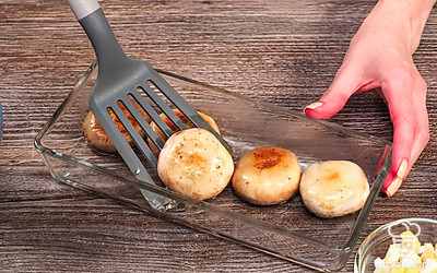 Подготовьте грибы. Сковороду поставьте на средний огонь. Обжарьте шляпки шампиньонов в смеси сливочного и растительного масла с обеих сторон по 1 минуте. Переложите шляпки на противень или в форму для запекания.