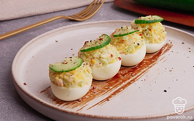 Выложите начинку в половинки яичных белков. Сверху украсьте яйца ломтиками свежего огурца. Украсьте тарелку бальзамическим кремом, выложите на нее фаршированные яйца и посыпьте все свежемолотым черным перцем. Готово. Приятного аппетита!